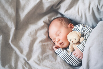 Newborn sleep at first days of life. Portrait of new born baby one week old with cute soft toy in crib in cloth background.