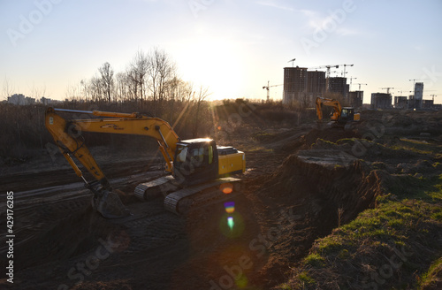 Excavator dig trench at construction site. Digging the pit foundation. Laying concrete sewer wells and sewer pipes. Sewage drainage system for multi-story buildings. Tower cranes in action