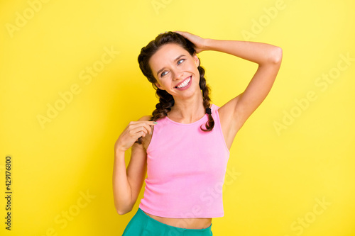 Photo of cute happy young woman look empty space summer mood touch hair braids isolated on bright yellow color background