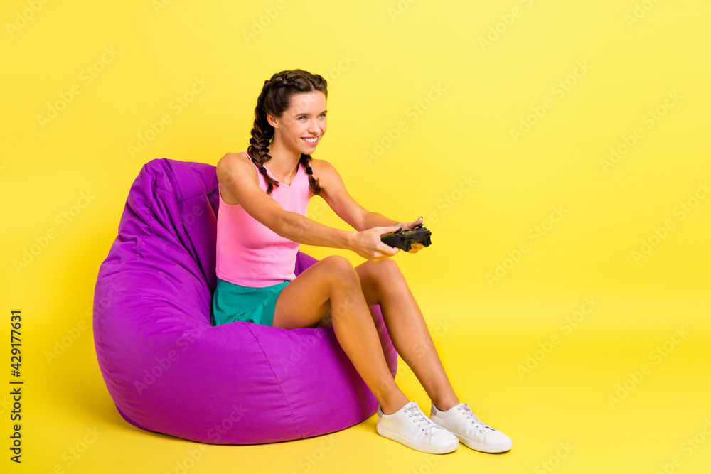 Full size profile side photo of charming concentrated lady hold joystick sit bean bag isolated on vibrant yellow color background Full size profile side photo of charming concentrated lady hold joystick sit bean bag isolated on vibrant yellow color background