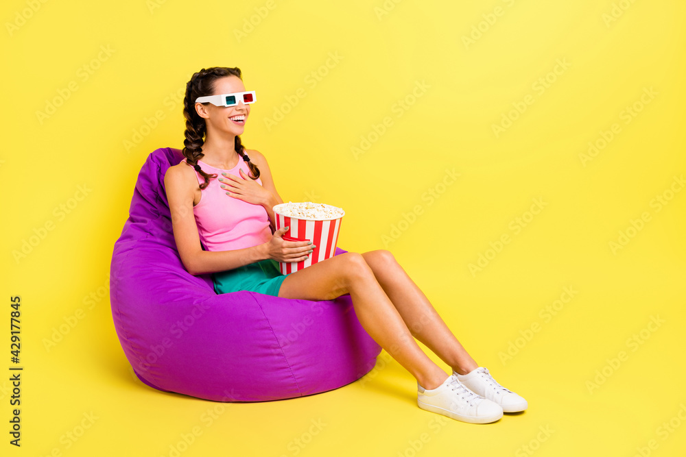 Full size profile photo of optimistic cool brunette lady sit watch film eat pop corn wear top skirt isolated on yellow color background