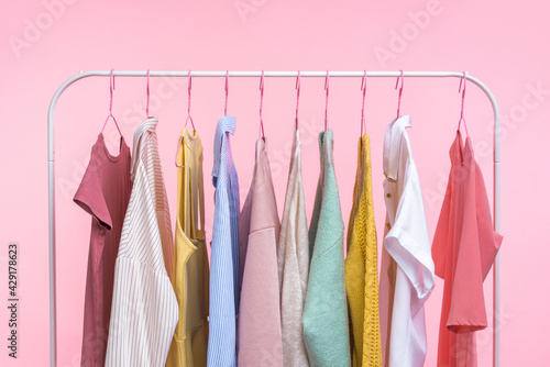 Collection of pastel colored women clothes hanging on rack in dressing room isolated on pink background