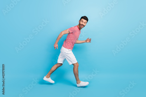 Full size profile side photo of cheerful positive young man walk run empty space isolated on pastel blue color background