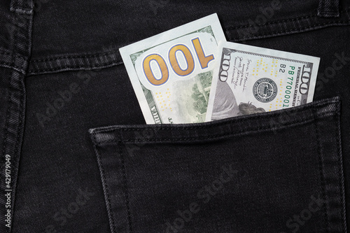 Two hundred dollar bills on different sides sticking out of a pocket of black jeans