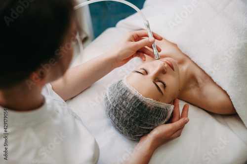 Upper view photo of a caucasian spa worker cleaning clients face with apparatus during skin care procedures photo