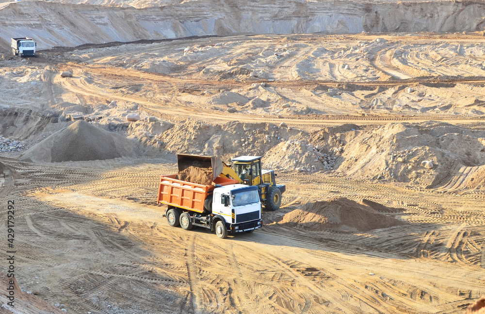 Wheel front-end loader loading sand into heavy dump truck at the opencast mining quarry. Dump truck transports sand in open pit mine. Quarry in which sand and gravel is excavated from the ground. Wheel front-end loader loading sand into heavy dump truck at the opencast mining quarry. Dump truck transports sand in open pit mine. Quarry in which sand and gravel is excavated from the ground.