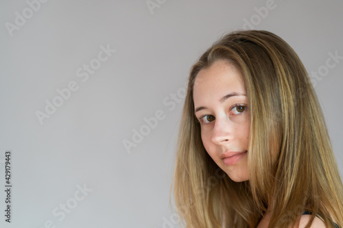 Close up studio portrait of a young back turned woman turning her head looking at the camera. Grey background