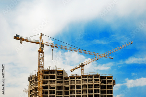 Two construction cranes against a blue sky background. Construction tower crane in yellow colour. Construction of a new building.