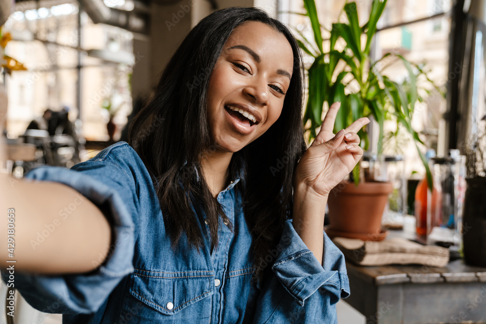 Black young woman smiling and taking selfie photo while sitting in cafe Black young woman smiling and taking selfie photo while sitting in cafe