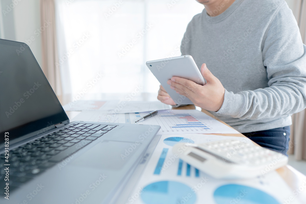 Businessman in casual wear stands beside desk to work at home with taplat. work from home. Businessman in casual wear stands beside desk to work at home with taplat. work from home.