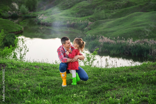 dad with little daughter in bright colored rubber boots on a walk by the lake on dad's day