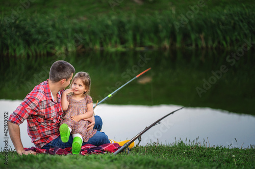 A little daughter sits in her father's arms while fishing. She listens carefully to his story.