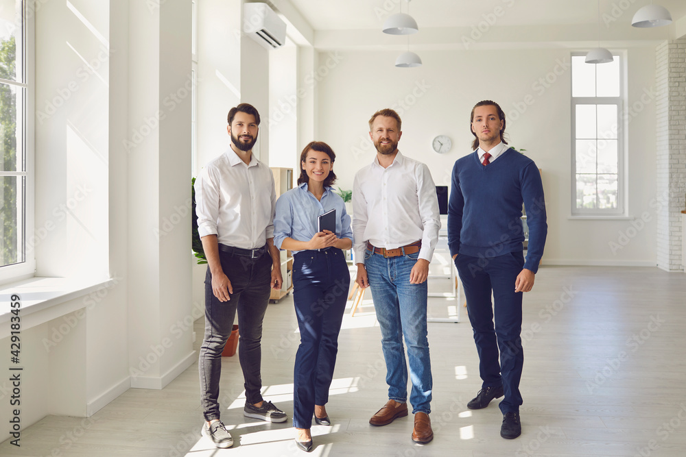 Fototapeta premium smiling business partners or project team standing and looking at camera in modern office