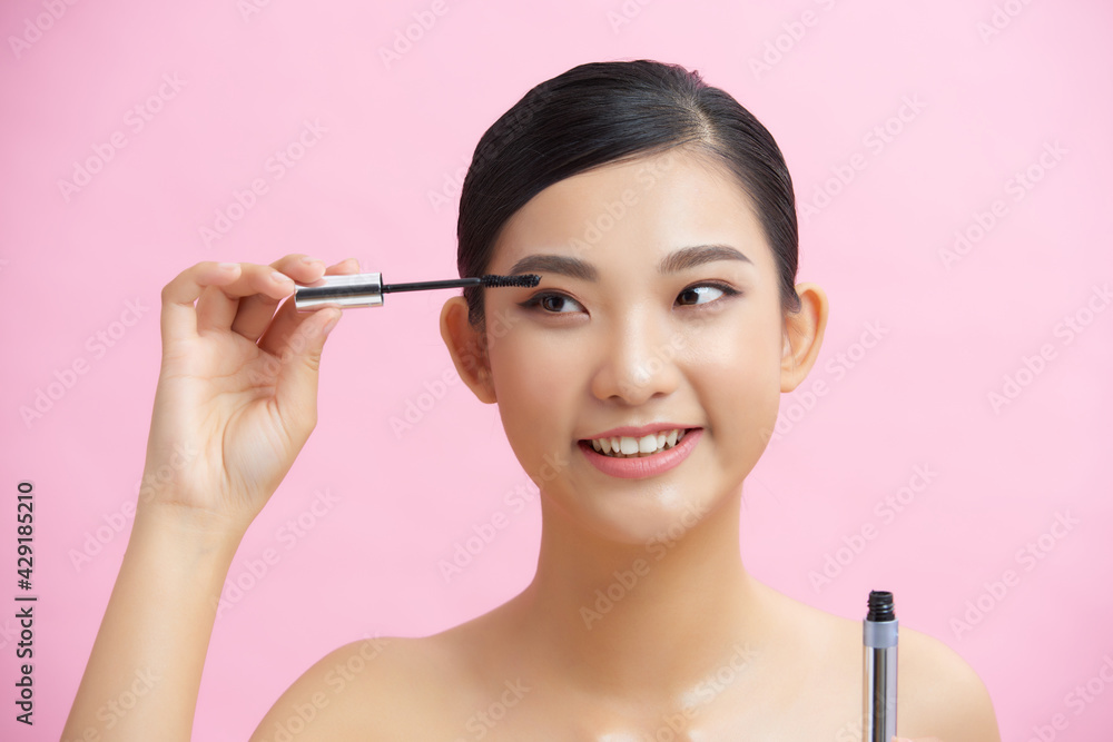 Fototapeta premium Beautiful woman mascara applying makeup natural portrait beauty concept over pink background