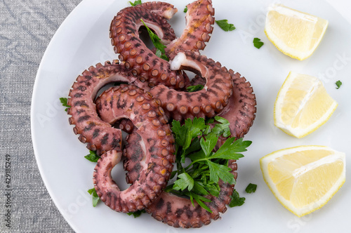 Grilled octopus accompanied by pieces of lemon and parsley on the white plate.