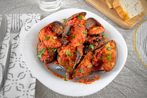 Stuffed mussels with tomato sauce and parsley on the white plate.