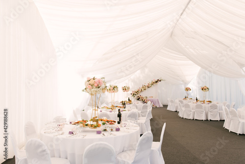 Luxury wedding dinner in a large beautiful tent, beautiful decor for the wedding of the white hall decorated with flowers