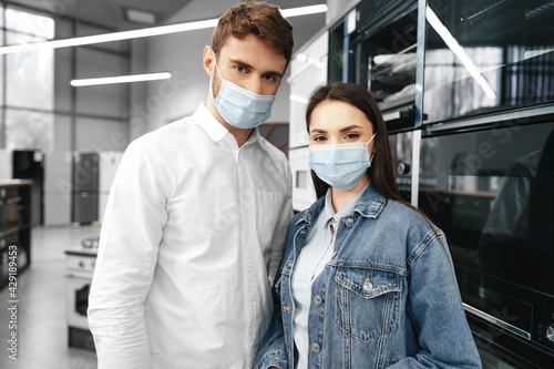 Young couple wearing medical masks in hypermarket with home appliances