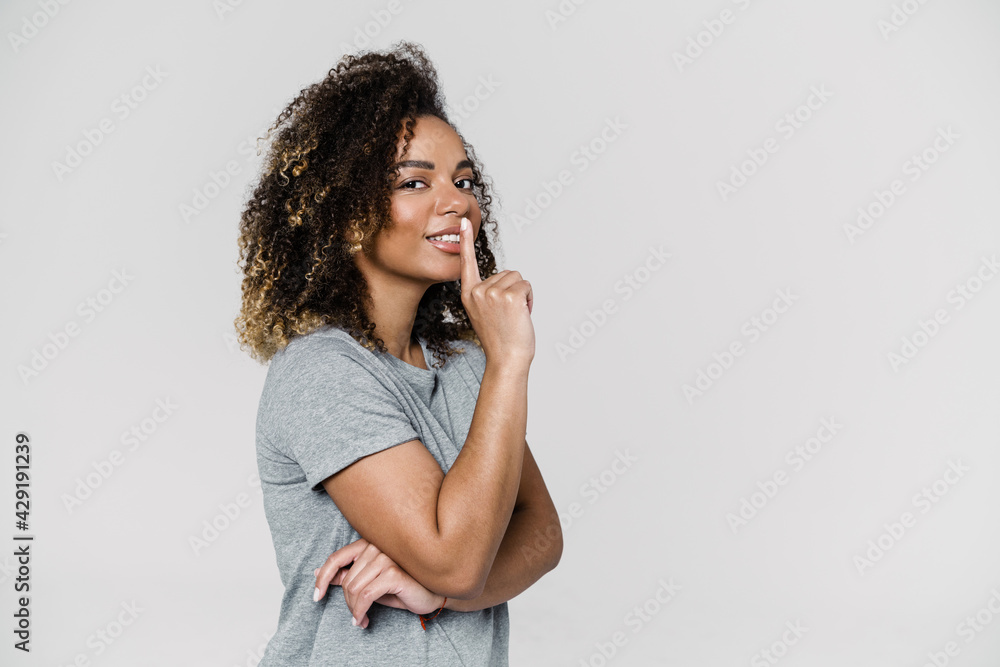 The side-view of a smiling woman showing silence gesture while standing in the studio The side-view of a smiling woman showing silence gesture while standing in the studio