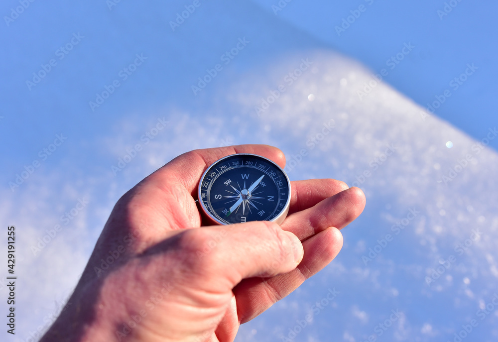 Compass in hand on snow background. Orientation on terrain in forest and mountain in winter time. Map reading and land navigation concept. Tourist compass and magnetic declination сalculator