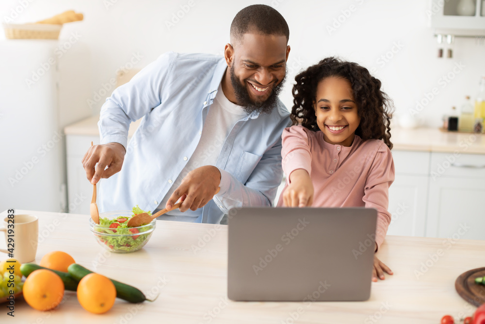Black man and girl cooking in kitchen reading online recipe Black man and girl cooking in kitchen reading online recipe