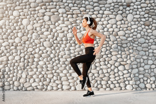 Sports woman dynamic movement jump pose against grey stone wall