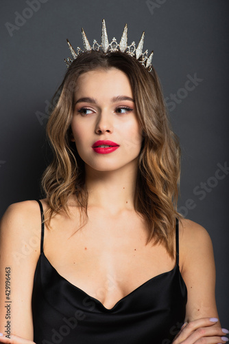 young woman in black slip dress and tiara with diamonds looking away on grey