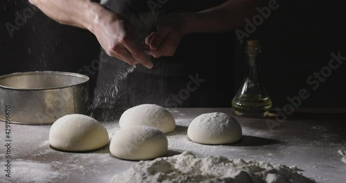 Chef prepares dough for traditional Italian pizza. Cooker sprinkles flour on dough in kitchen, 4k footage