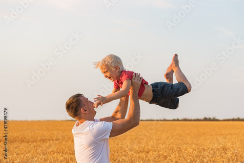 Father playing with son outdoors in field. Daddy tosses child up photo