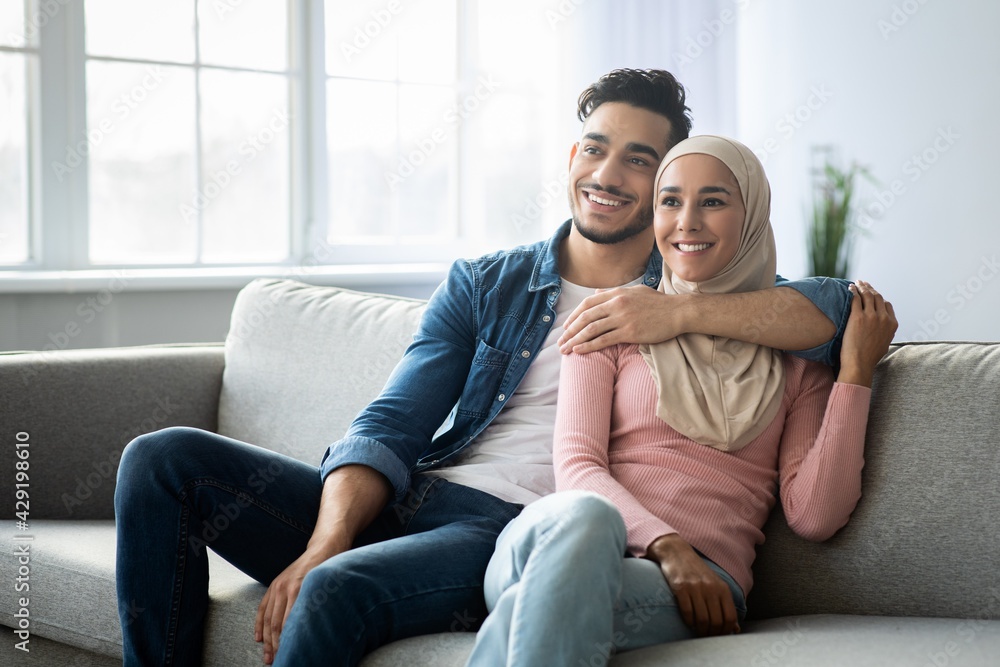 Obraz premium Positive arab couple sitting on couch at home