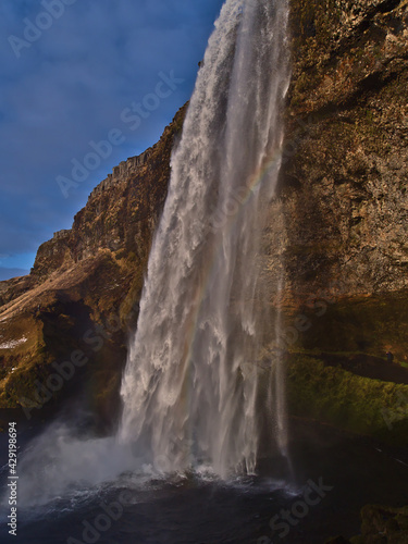 Beautiful side view of famous waterfall Seljalandsfoss on the southern coast of Iceland near ring road with colorful rainbow in between in the evening sun in winter season.