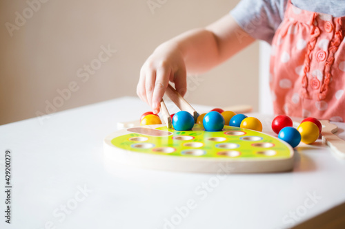 Bild auf Leinwand small baby lays out balls with tweezers in holes