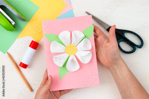 A flower made of cotton pads. Colored paper, stapler, scissors, scissors, pencil on a white table. Children's craft card for mother's day. Step-by-step instruction. Step 10.