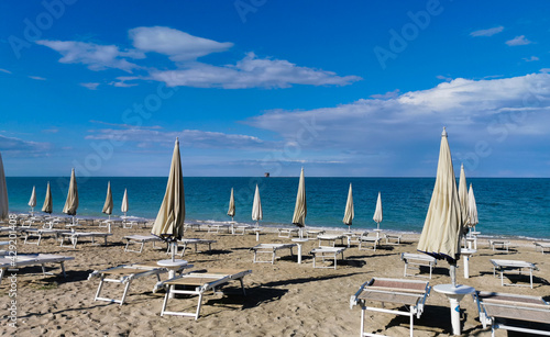 Ombrelloni e lettini sulla spiaggia vuota e piattaforma sul mare all’orizzonte © GjGj