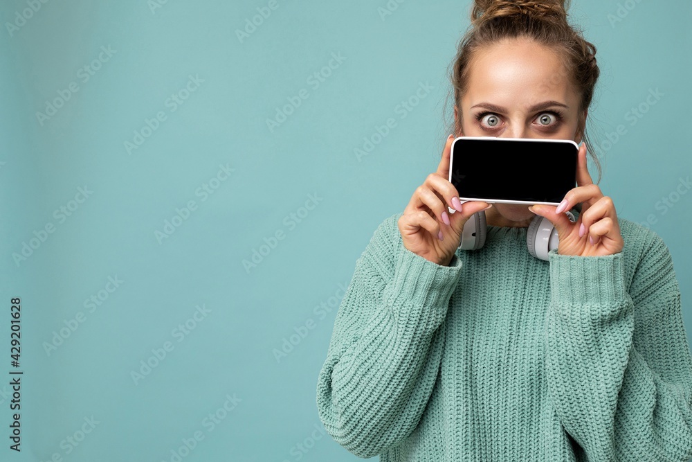 Photo of beautiful young woman good looking wearing casual outfit standing isolated on background with copy space holding smartphone showing phone in hand with empty screen display for mockup looking