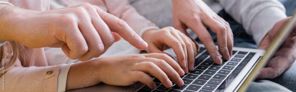 Cropped view of man pointing at laptop near wife and daughter, banner. Cropped view of man pointing at laptop near wife and daughter, banner.
