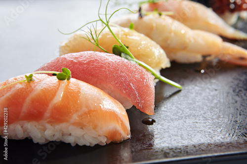 Japanese Nigiri Sushi Set - Sushi with Rice and Various Seafood. Salmon, Tuna, Sea Scallop and other seafood fish. Nigiri Sushi row on black slate platter. Isolated on white background.
