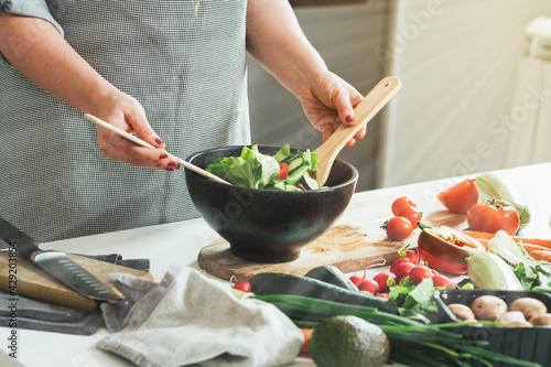Close up photo of woman hands making fresh salad. Housewife making lunch  mixing organic vegetables with mixing spoon at kitchen with sun rays in home