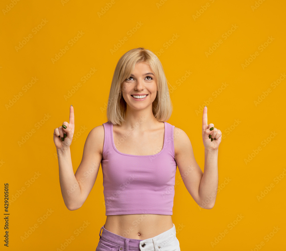 Amazing offer. Happy woman pointing two index fingers up at free space above her head over yellow background, crop Amazing offer. Happy woman pointing two index fingers up at free space above her head over yellow background, crop