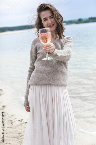 young beautiful brunette woman drinking rose wine in a glass on the street, wine tasting near the water, lake or sea