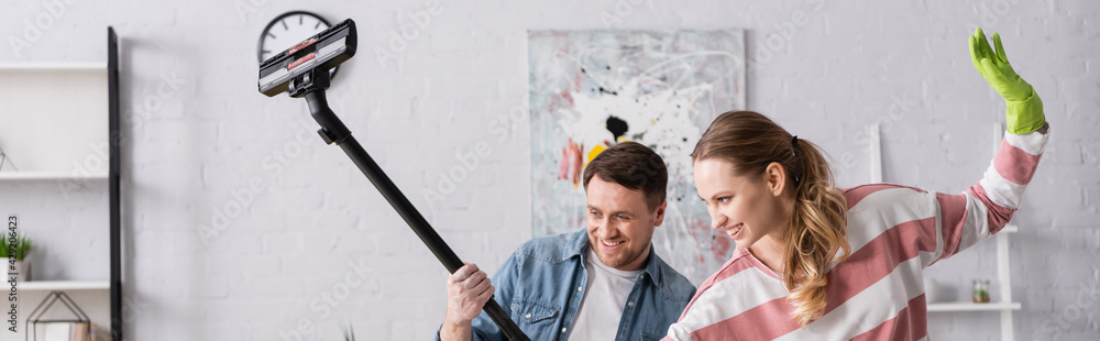 Woman in rubber glove standing near cheerful husband with vacuum cleaner, banner. Woman in rubber glove standing near cheerful husband with vacuum cleaner, banner.
