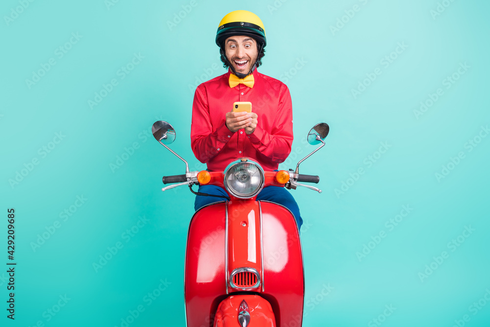 Fototapeta premium Photo of impressed brunette guy ride on bike hold telephone wear red shirt helmet isolated on teal color background