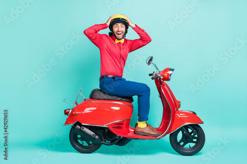 Full size profile side photo of amazed man wear red shirt blue pants ride bike hands head isolated on teal color background