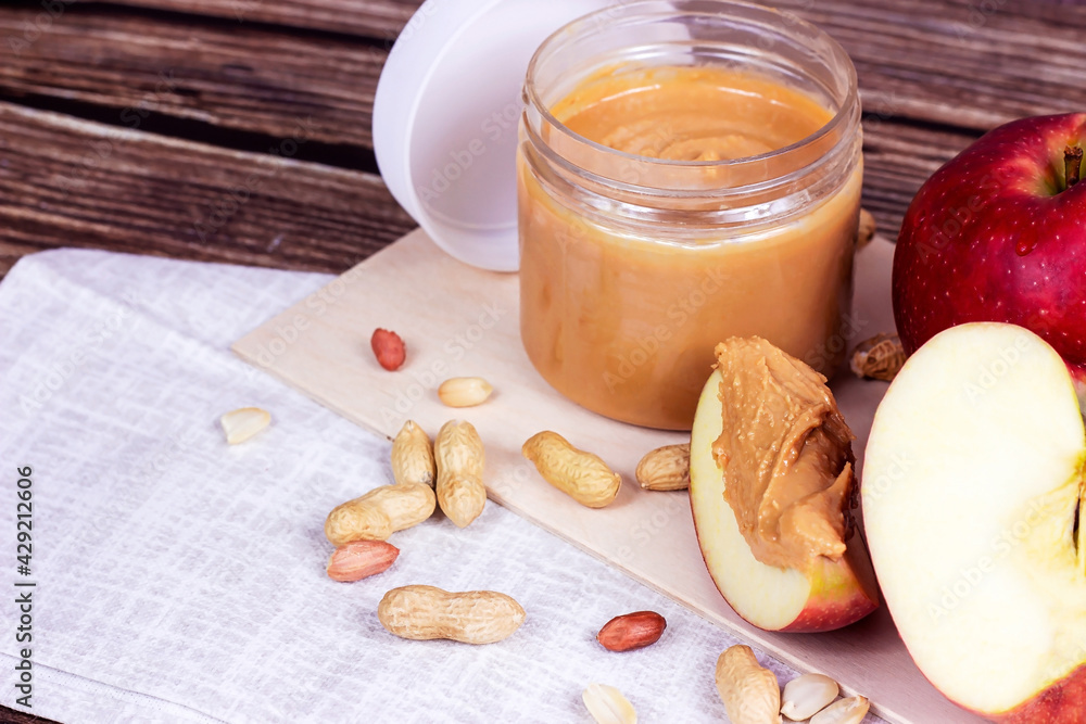 Fresh homemade crunchy peanut butter with nuts and apples on light wooden background in the kitchen. Fresh homemade crunchy peanut butter with nuts and apples on light wooden background in the kitchen.