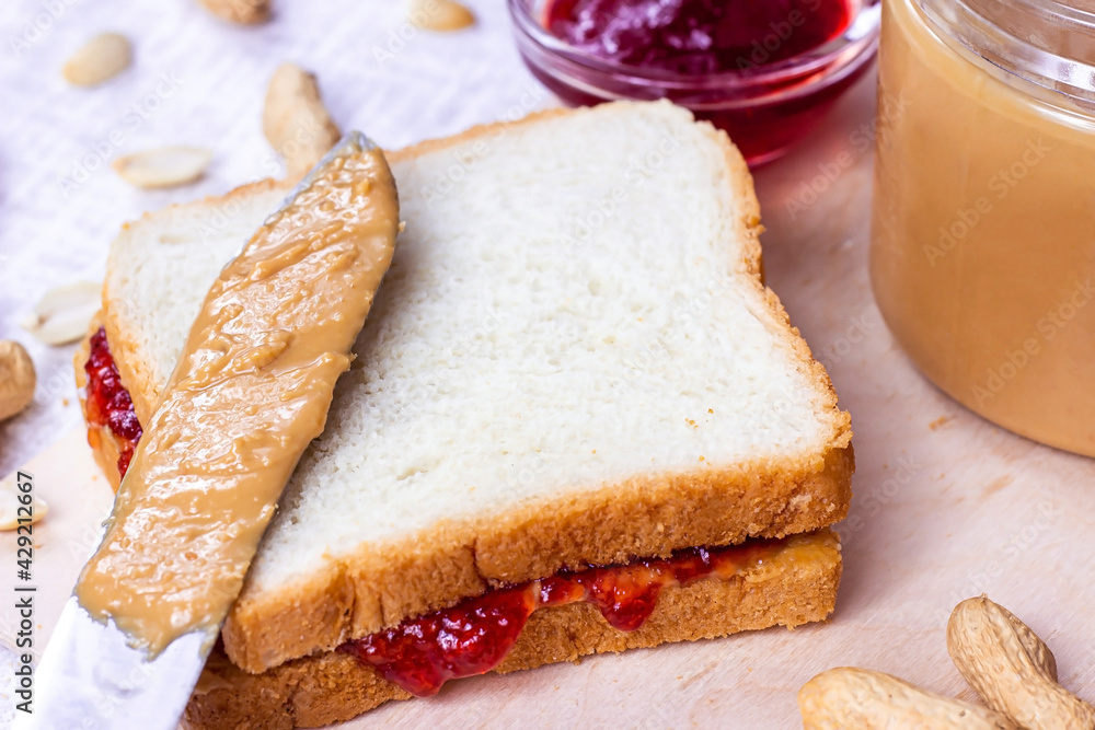 Homemade sandwich for breakfast with fresh crunchy peanut butter and strawberry jelly on light background.