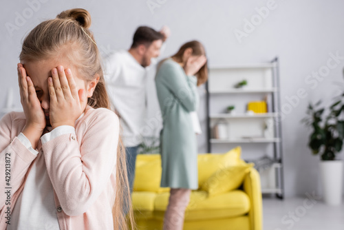 Girl covering face while father yelling on mother on blurred background.