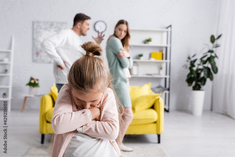 Displeased kid with crossed arms standing near father quarreling with mother.