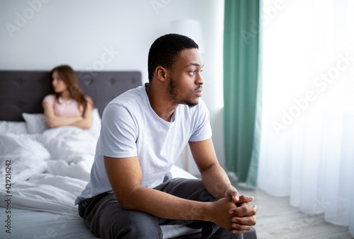 Relationship crisis. Young black man feeling upset after fight with his wife, sitting on bed at home photo