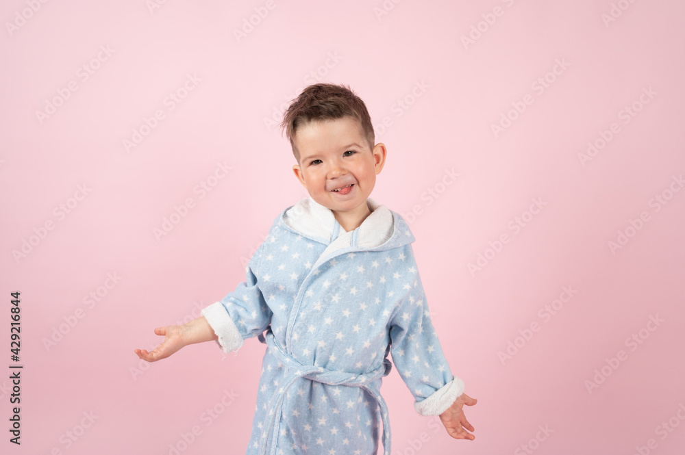 Portrait of caucasian kid boy in bathrobe on pink background. Funny boy shows his tongue Portrait of caucasian kid boy in bathrobe on pink background. Funny boy shows his tongue