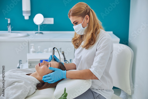 Obraz na plátně Beautiful elegant doctor in white uniform doing skin care for pretty lady in bea